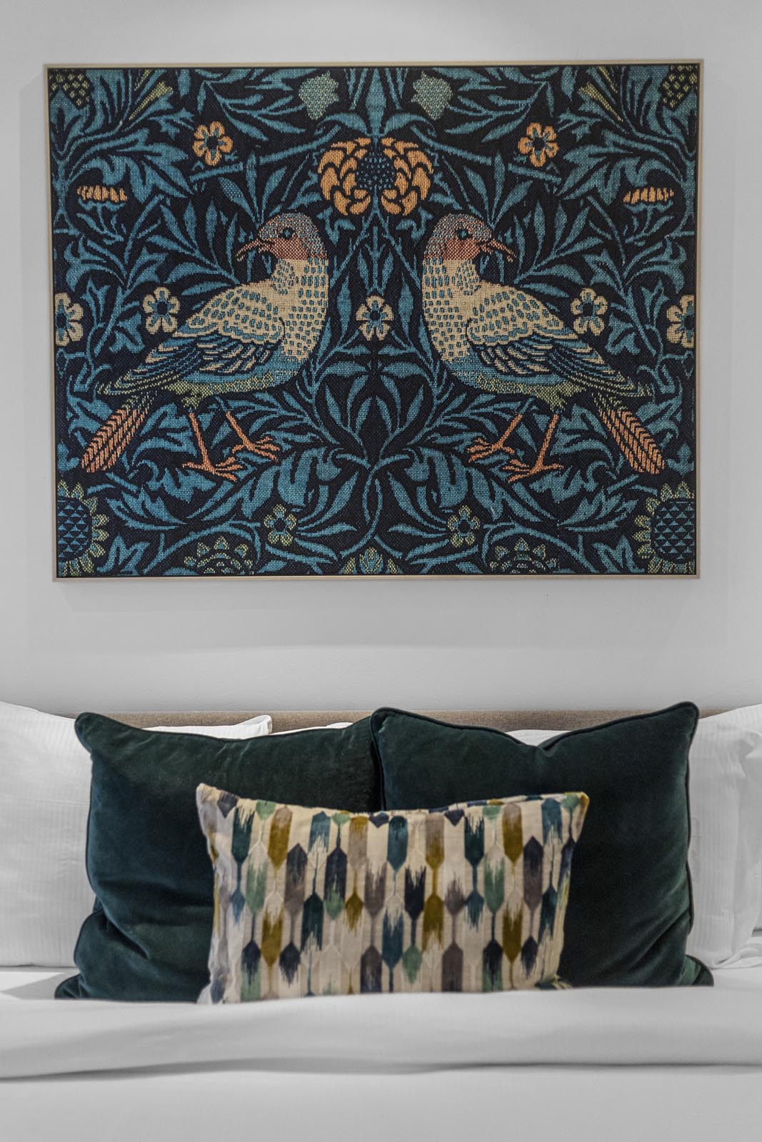 Bedroom styling detail photography: bird-print artwork above teal velvet cushions