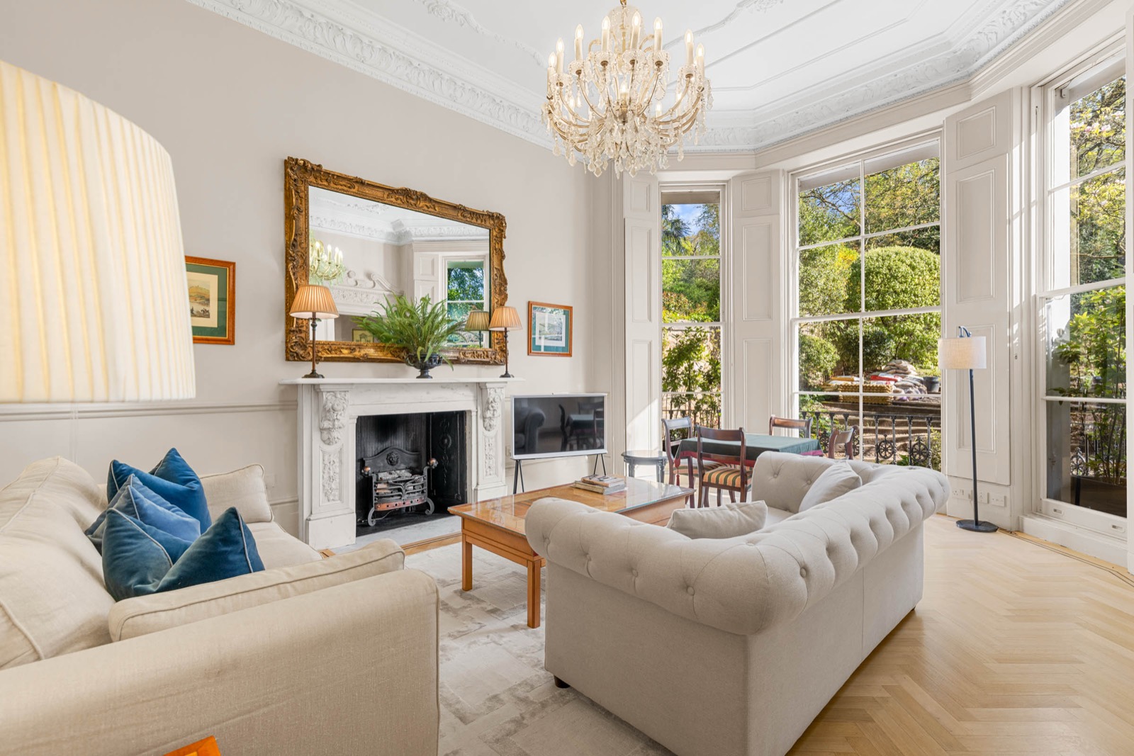 Living room photography in a Kensington mansion flat: chandelier, Chesterfield sofa and bay windows onto the garden