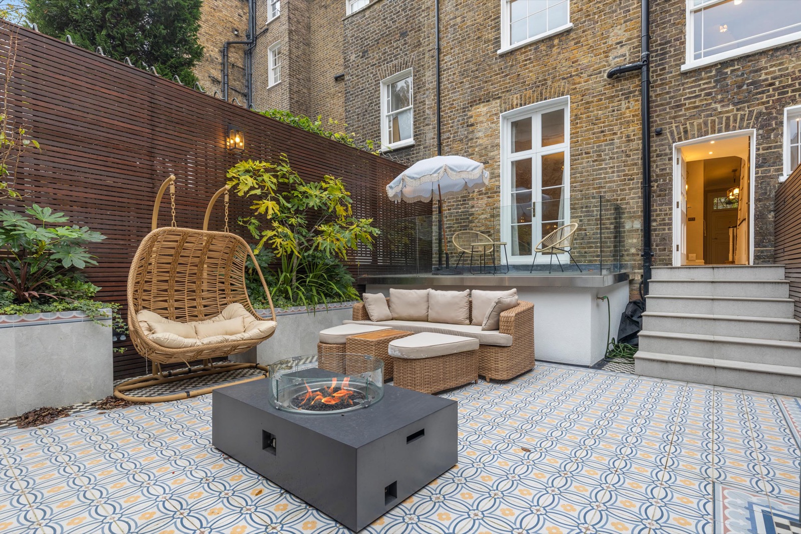 Garden terrace photography of a Victorian house in Hampstead: hanging egg chair, fire pit and patterned tiles