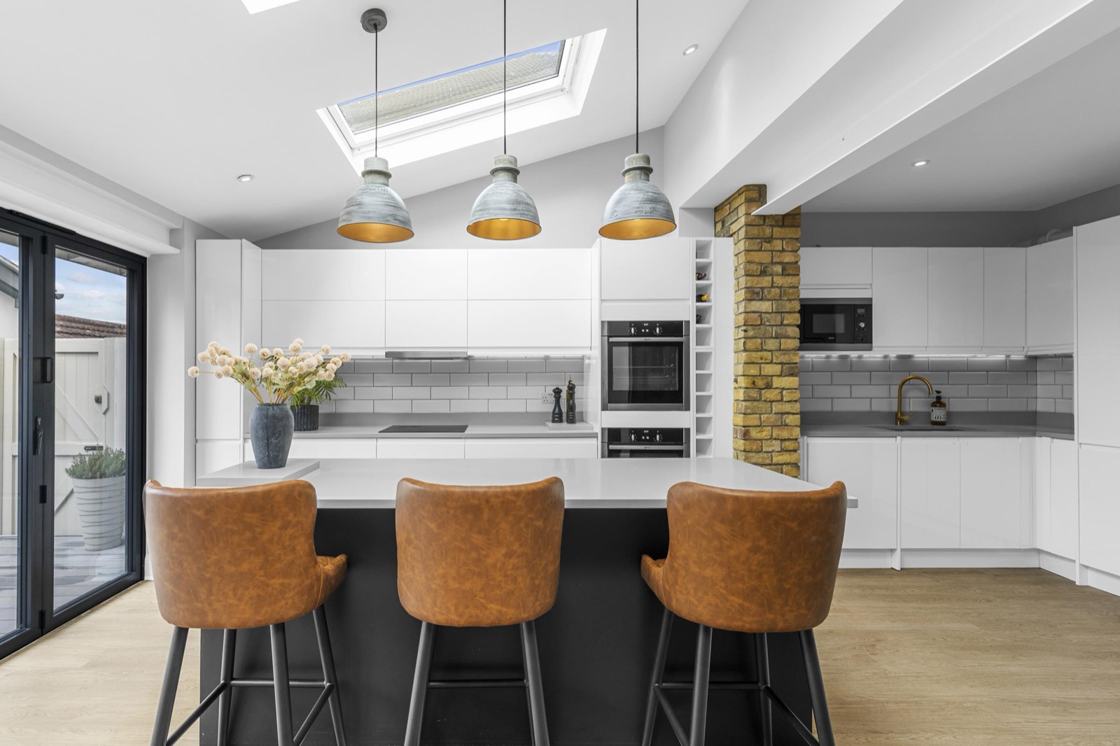 Kitchen extension photography in a Fulham home: island with leather stools, pendant lights and skylight