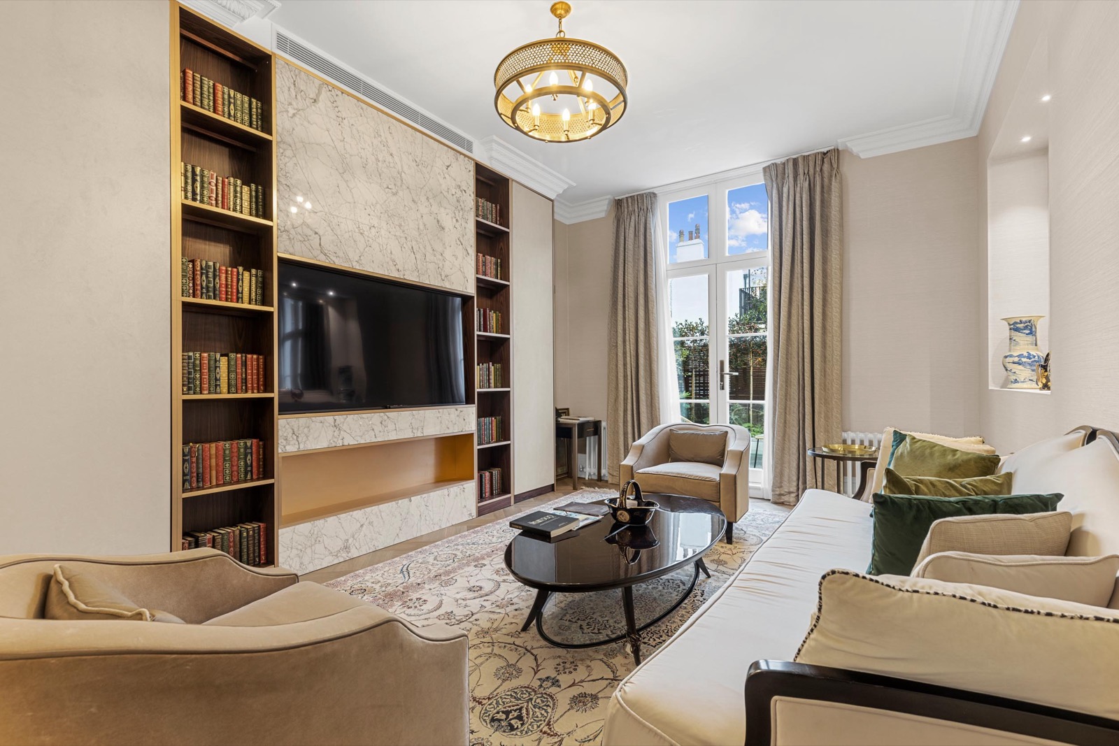 Living room photography in a Belgravia apartment: built-in library shelves, brass chandelier and tall windows